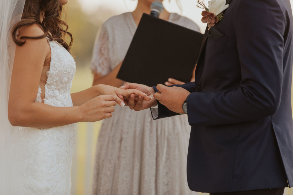 Close-up of a bride and groom exchanging wedding rings during an outdoor ceremony at The Pavilion at Haggin Oaks in Sacramento.