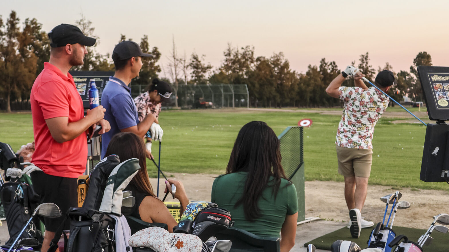 Group of friends enjoying golf, drinks, and food while practicing at The Hangout driving range at Haggin Oaks Golf Complex in Sacramento.