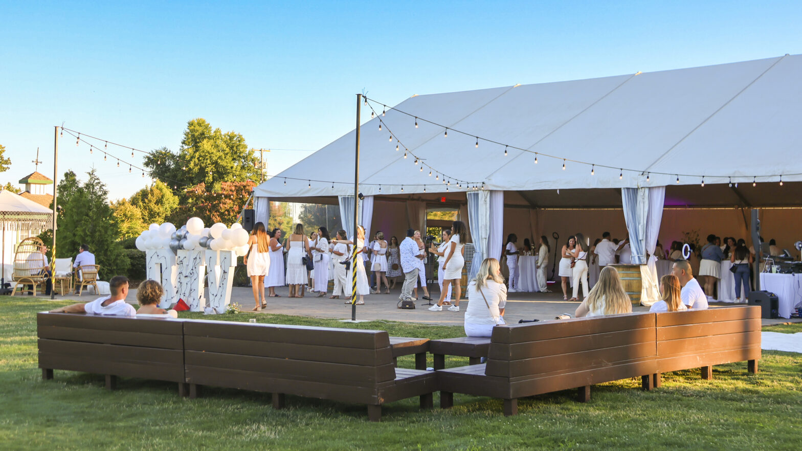 Outdoor private event at The Pavilion at Haggin Oaks featuring guests gathered around the reception tent, lawn seating, string lights, and open-air event space in Sacramento.