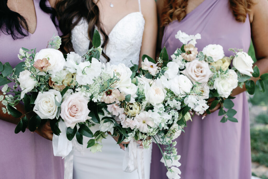 Bride and bridesmaids holding white and blush floral bouquets during wedding preparations at The Pavilion at Haggin Oaks in Sacramento.