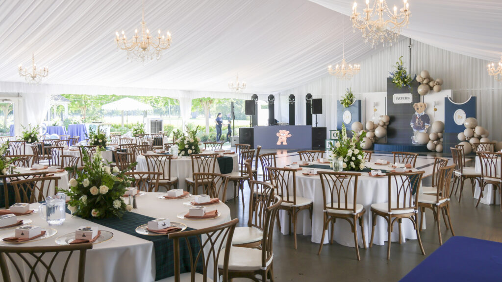 Fundraising gala setup inside a white event tent at The Pavilion at Haggin Oaks featuring banquet tables, floral centerpieces, chandeliers, and a presentation stage in Sacramento.