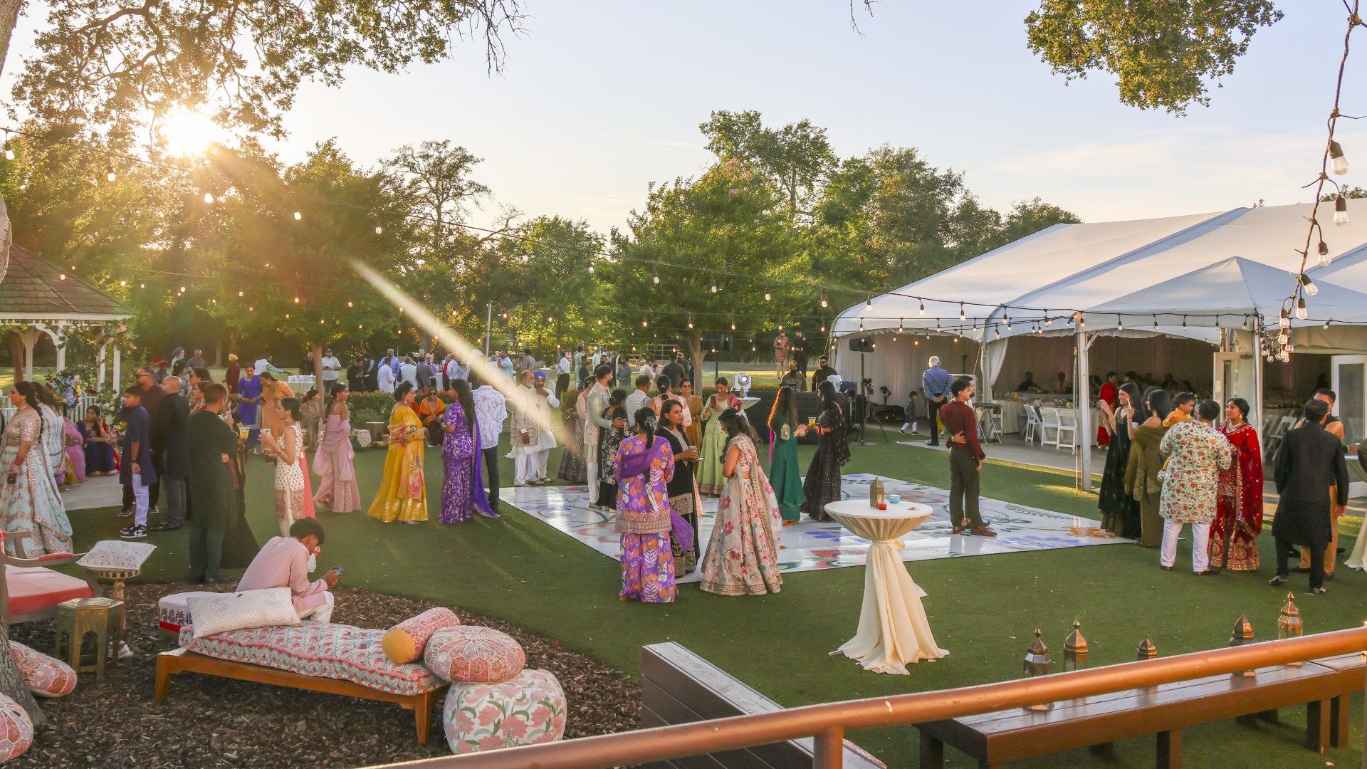 Outdoor cultural wedding celebration at The Pavilion at Haggin Oaks featuring guests in traditional attire, lounge seating, string lights, and a reception tent during a Sacramento event.