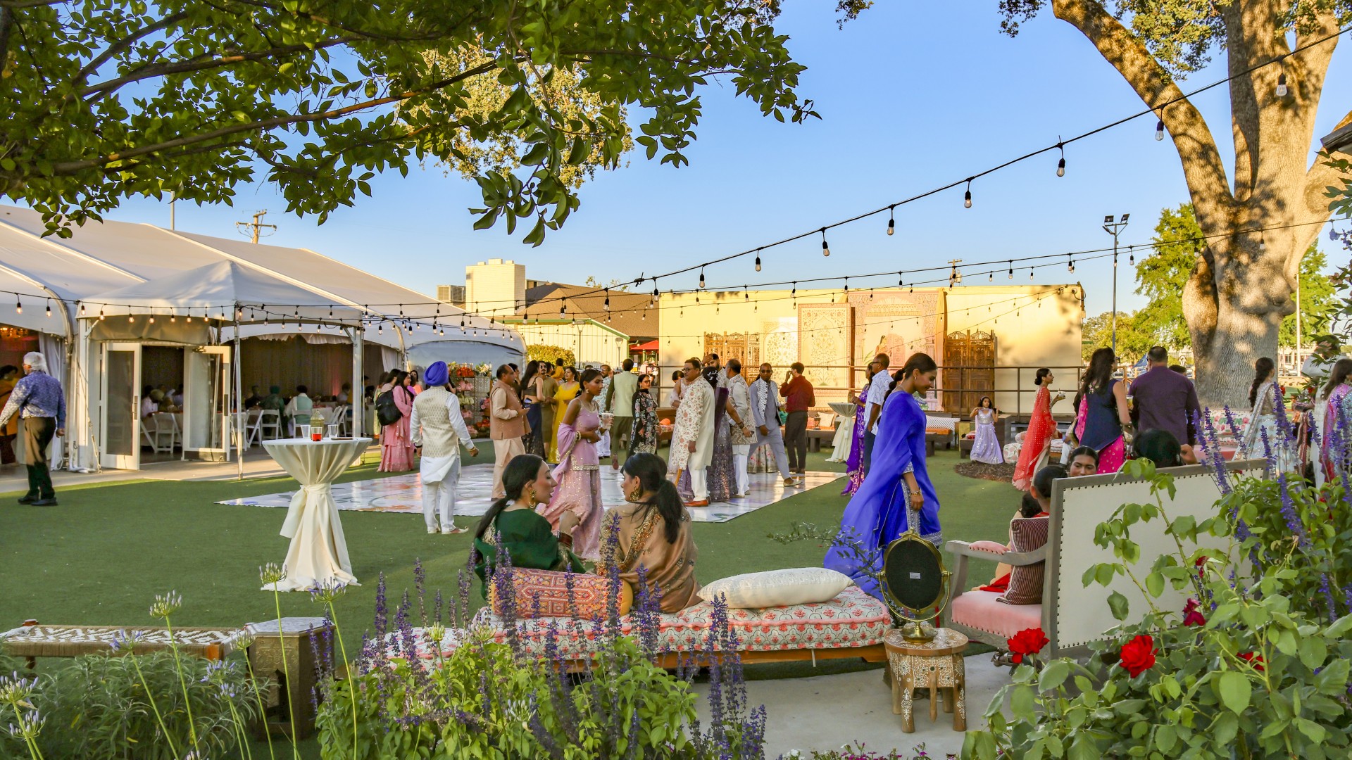Outdoor cultural wedding celebration at The Pavilion at Haggin Oaks featuring guests in traditional attire, lounge seating, string lights, a reception tent, and garden gathering spaces in Sacramento.