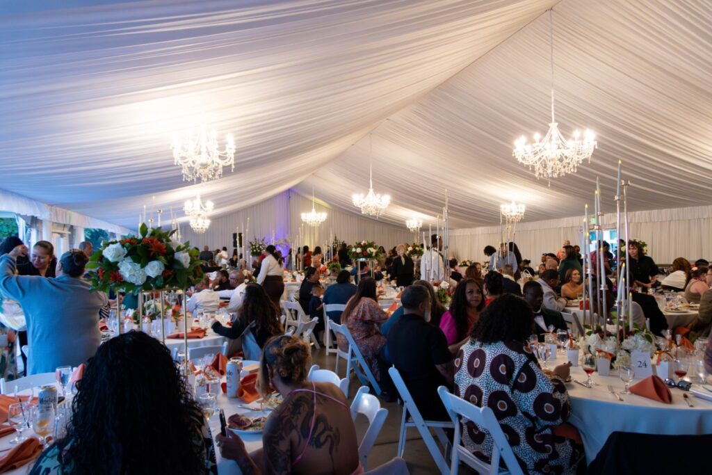 Wedding reception inside a white event tent at The Pavilion at Haggin Oaks featuring banquet tables, floral centerpieces, chandeliers, and guests celebrating during an evening event in Sacramento.