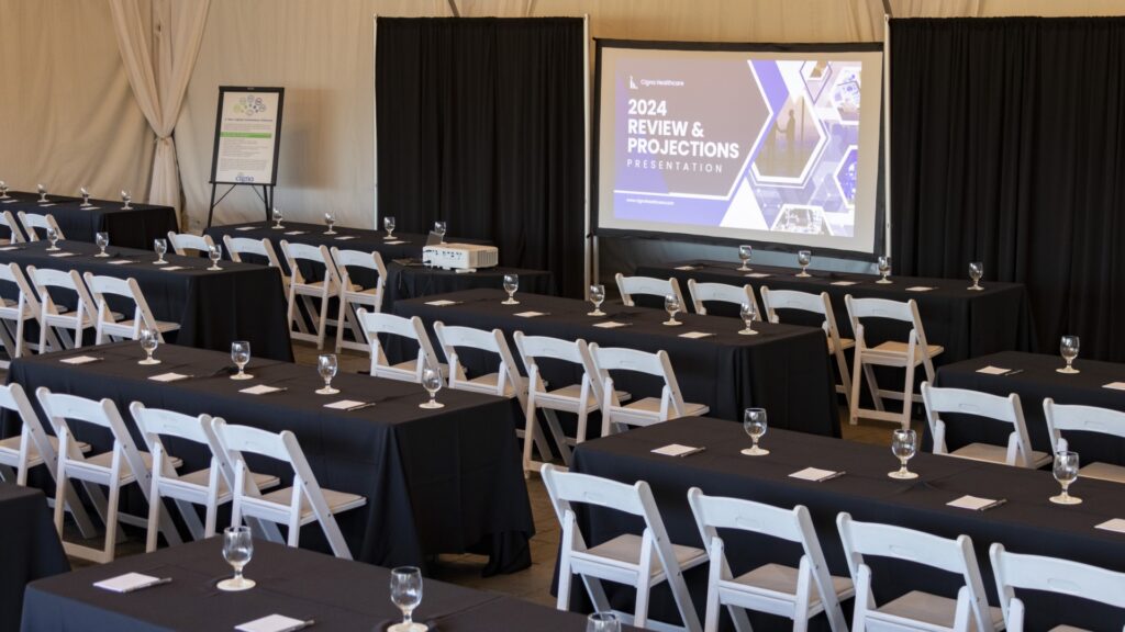 Corporate meeting setup inside an event tent at The Pavilion at Haggin Oaks featuring classroom-style seating, presentation screen, projector, and conference tables in Sacramento.