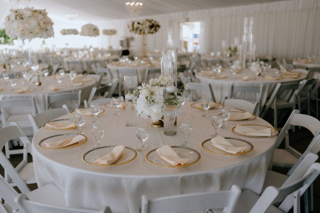 Wedding reception tables with floral centerpieces, gold-rimmed place settings, and banquet seating inside The Pavilion at Haggin Oaks, prepared for a Sacramento wedding celebration.