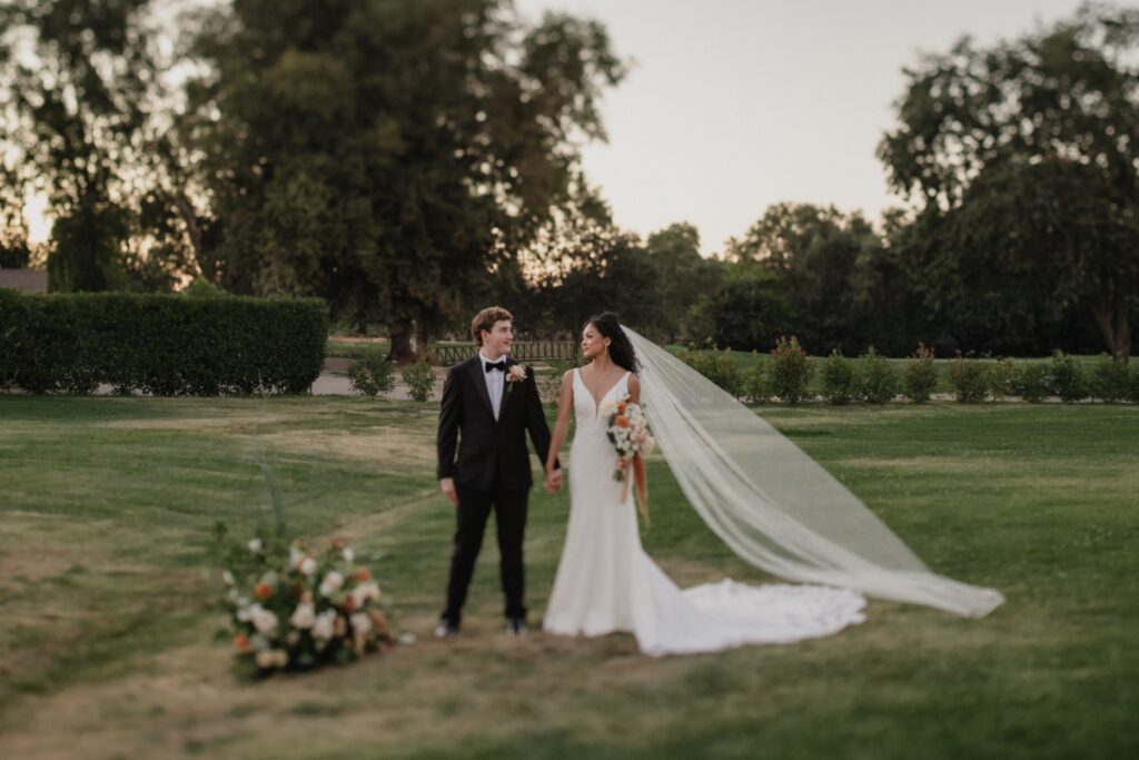 Bride and groom holding hands on the golf course at The Pavilion at Haggin Oaks with a flowing wedding veil and sunset scenery in Sacramento.