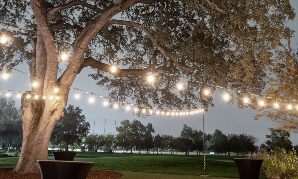 Elegant wedding reception venue at The Pavilion at Haggin Oaks featuring round banquet tables, floral centerpieces, soft lighting, and panoramic golf course views through large windows in Sacramento.