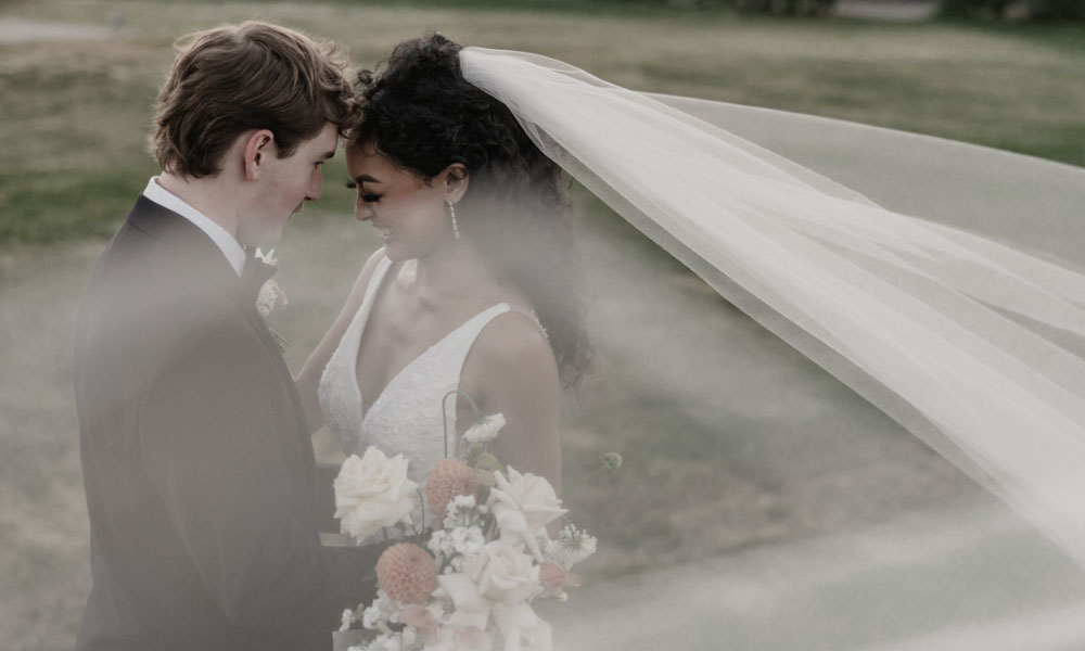 Bride and groom sharing a romantic moment outdoors at The Pavilion at Haggin Oaks with elegant wedding attire, lush greenery, and scenic golf course views in Sacramento.