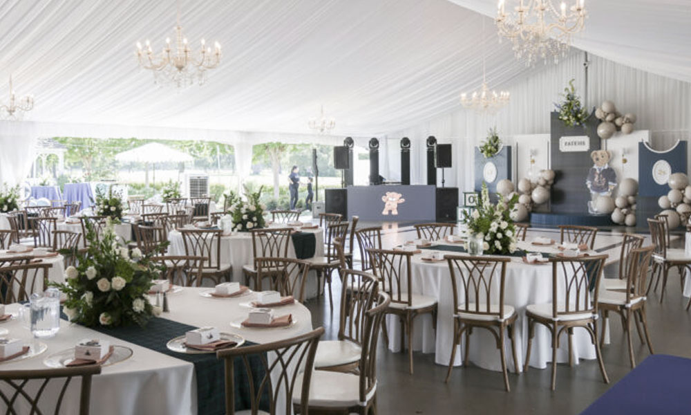 Elegant wedding reception setup inside The Pavilion at Haggin Oaks featuring round guest tables, white linens, floral centerpieces, chandeliers, and large windows overlooking the golf course in Sacramento.