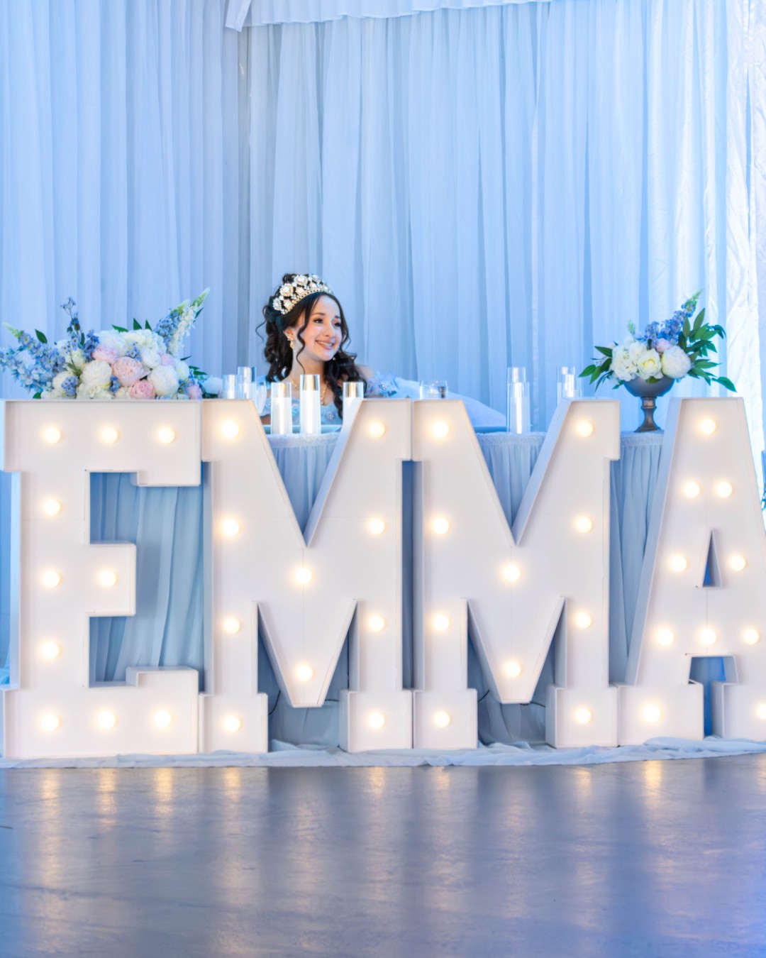 Young woman seated at a decorated head table with illuminated marquee letters spelling her name, floral arrangements, and event décor during a quinceañera celebration at The Pavilion at Haggin Oaks in Sacramento.