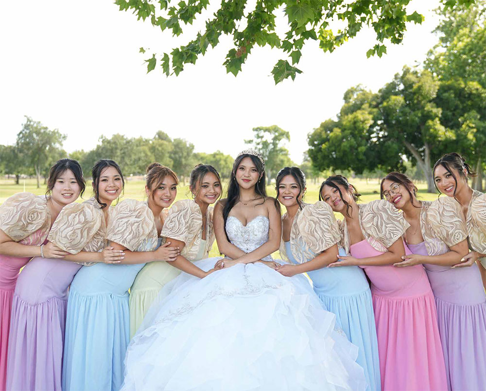 Young woman in a formal quinceañera gown posing with her court in colorful dresses on the golf course at The Pavilion at Haggin Oaks in Sacramento.