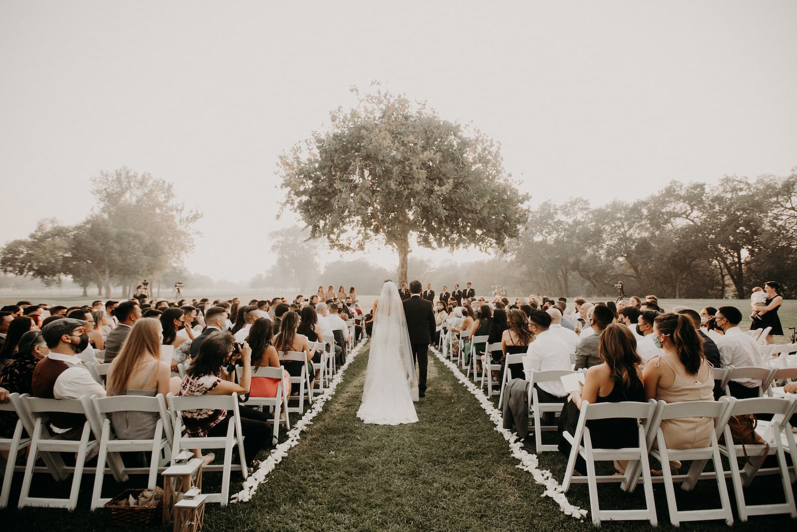 Outdoor wedding ceremony at the Pavilion at Haggin Oaks with the bride and groom walking down the aisle surrounded by guests.