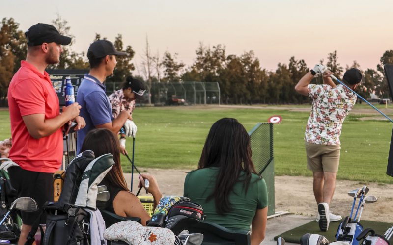 Group of friends enjoying golf, drinks, and food while practicing at The Hangout driving range at Haggin Oaks Golf Complex in Sacramento.